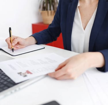 An HR specialist in blue blazer writing notes while reviewing a resume at a white desk 
