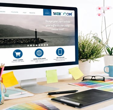 Desktop computer displaying a website builder tool on a creative office desk with design supplies.