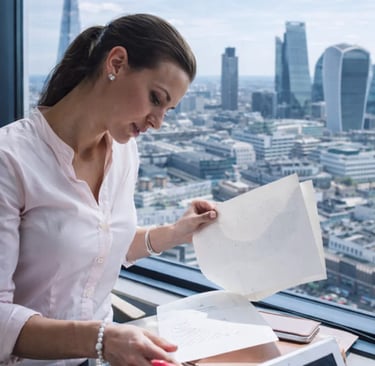 A professional businesswoman reviews documents in a high-rise London office overlooking the city skyline.