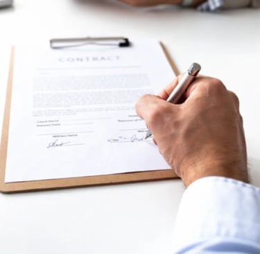 A businessman signs a legal business contract on a clipboard with a silver pen on a white desk.