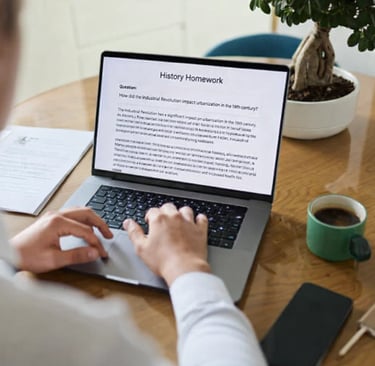 Copywriter typing a history homework assignment on a laptop at a wooden desk with coffee.