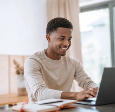 Smiling young Black man working on a laptop at a desk, focused on remote work and digital learning.