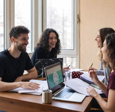 Diverse group of smiling university students studying together with laptops and notebooks at a table.