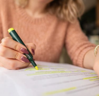 A student using a yellow highlighter to mark important notes on a written document, during revision 