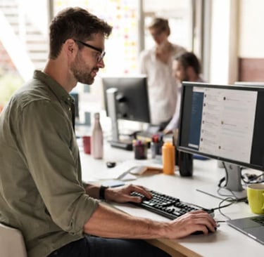Professional copywriter working on a desktop computer in a modern open-plan office space.