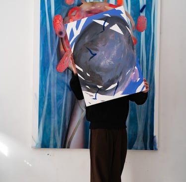 Artist in a studio holding a contemporary abstract painting over their face in front of a larger blue canvas.