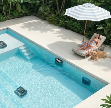 Automatic robotic pool cleaners working in a luxury swimming pool while a woman relaxes nearby.