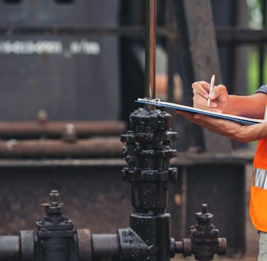 Plumber in safety vest inspecting industrial drain pipes and taking notes on a clipboard
