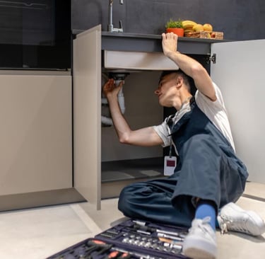 Plombier accroupi sous un évier de cuisine moderne inspectant les tuyaux de drain lors d'entretien