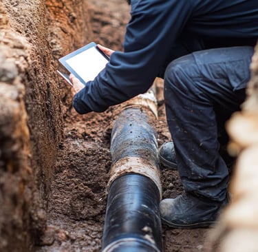 Technician using a tablet to inspect an underground drainage pipe during preventive maintenance