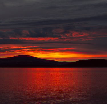 a sunset over a lake with a mountain in the background