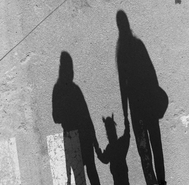 Schaduw van ouders met kind tussen hen in, lopend over straat. Symbolisch voor verbinding.