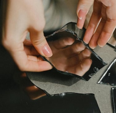 Hand pakt spiegelscherf op: reflectie komt stukje bij beetje, tot je het geheel ziet.