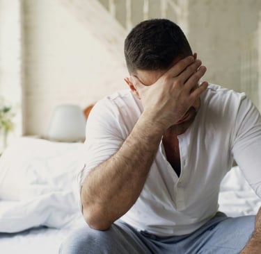 Stressed man sitting on bed with head in hand during a relationship conflict.