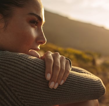 A woman in a knit sweater looking at a mountain sunset during a nature hike.