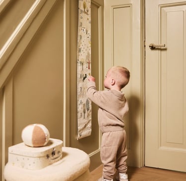 A young toddler looking at a height chart, in a Jollein photoshoot
