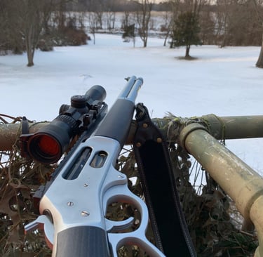 A lever action hunting rifle with a scope resting on a snowy field overlook for winter hunting.