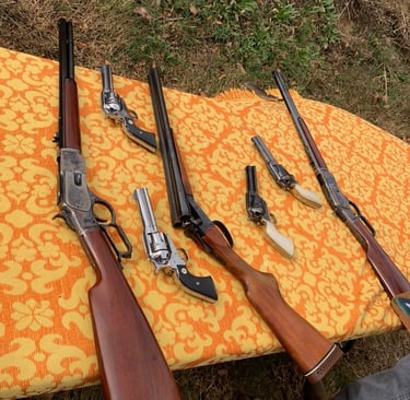 Collection of Western-style firearms including lever-action rifles, revolvers, and a double-barrel shotgun on a blanket.