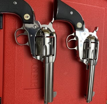 Two Ruger Vaquero stainless steel single-action revolvers resting on a red textured handgun case.
