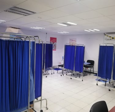 Sala de exámenes médicos con cubículos separados por cortinas azules, diseñada para brindar privacid