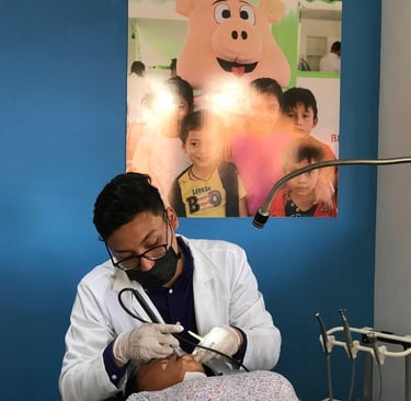 Odontólogo realizando un procedimiento dental a un paciente, con un póster infantil decorativo al fo