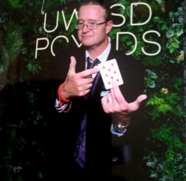 Professional magician in a suit performing a card trick with a nine of diamonds at an event.