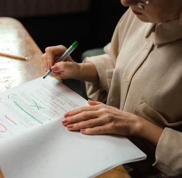 a woman in a brown shirt is writing and editing on a piece of paper