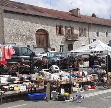 Outdoor flea market stalls with used clothing and household goods in front of a stone building.