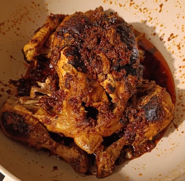 A spicy whole roasted chicken coated in red chili oil and aromatic spices in a white ceramic pan.