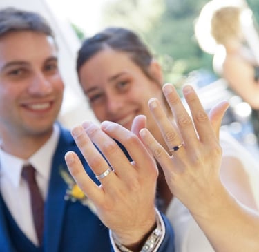 Photo de coule de jeunes mariés montrant leurs alliances avec le sourire.