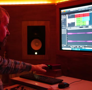 Luke Stidworthy sitting at a desk with a keyboard and a computer monitor editing music
