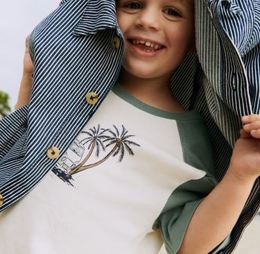 Marketing photo from Wheat childrenswear showing a blond boy with a striped jacket over his head