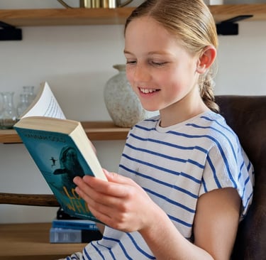 Smiling young girl with braided hair reading a children's book at home titled The Lost Whale.