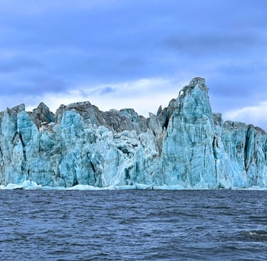 Massive blue glacier ice wall towering over dark ocean water under a cloudy sky.
