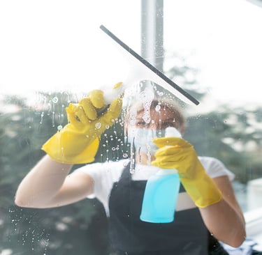 a woman in a black apron and yellow gloves cleaning a window
