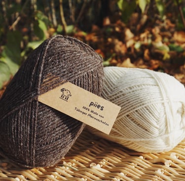 zwei Wollknäuel der Marke piies, einmal hell und einmal dunkel