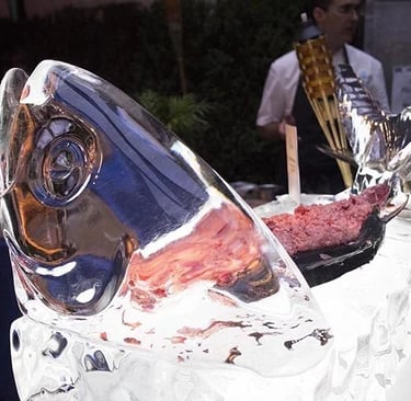 A decorative fish ice sculpture serving fresh tuna tartare at a catered outdoor event.