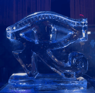 A detailed ice sculpture of the Egyptian Eye of Horus glowing with blue light in a dark room.
