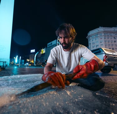 Artist carving a large block of ice at night with the Obelisk of Buenos Aires in the background.