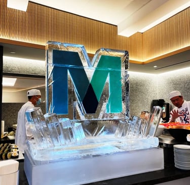 A decorative blue letter M ice sculpture centerpiece at a luxury buffet with sushi chefs.