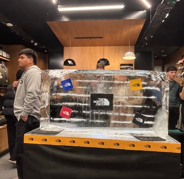 A branded The North Face ice sculpture display inside a retail store with customers browsing outdoor apparel.