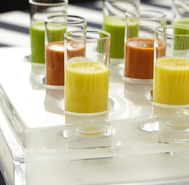 Colorful vegetable soup shooters in small glass cups on a clear acrylic serving tray.