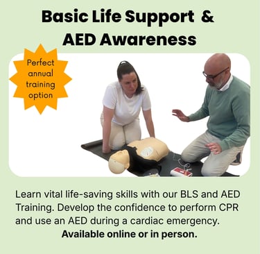Two people knelt on the floor at the side of a training CPR manikin, defibrillator pads are attached