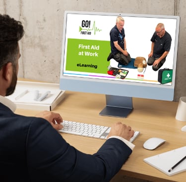 a man at a computer desk looking the computer screen showing a first aid course