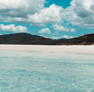 Pristine white sand beach with turquoise ocean water under a cloudy blue sky in the Whitsundays.