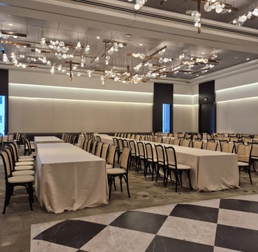 Modern banquet hall setup with long tables, neutral décor, and contemporary chandelier lighting