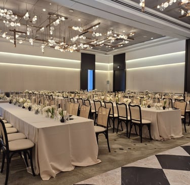 Elegant banquet hall setup with long tables, white floral arrangements, and modern chandelier