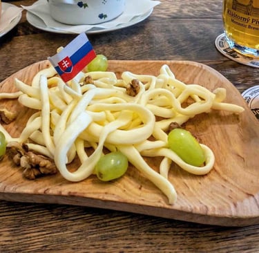 Aperitivo típico eslovaco servido en una tabla de madera sobre una mesa rústica, con una cerveza