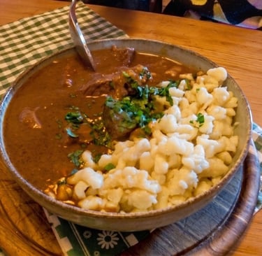 Cuenco de gulasch vienés (estofado de carne) con salsa oscura, servido con pasta spätzle y perejil