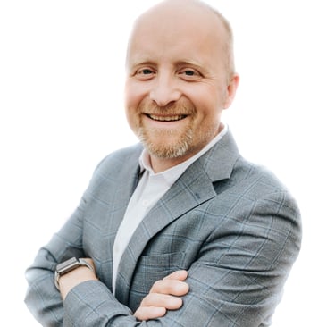 A white man with a blonde goatee. He's wearing a bright shirt and a light grey suit.
